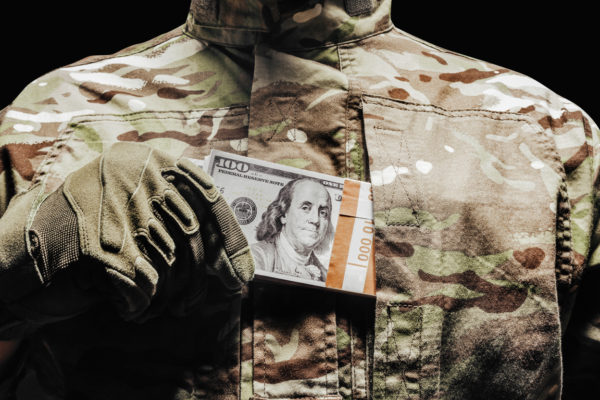 Photo of a soldier in camouflage and tactical gloves putting money in pocket.